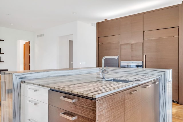 kitchen with light stone counters, sink, an island with sink, and light hardwood / wood-style floors