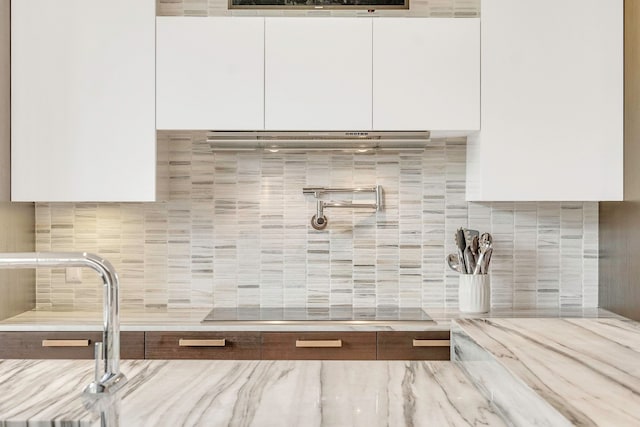 details with tasteful backsplash, white cabinetry, black electric stovetop, and ventilation hood