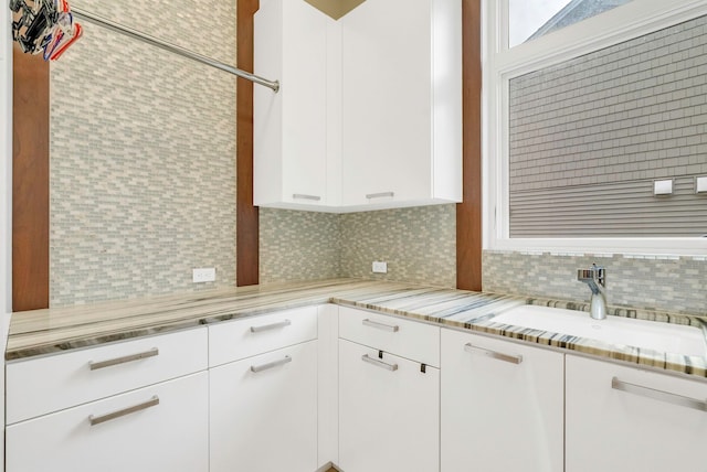 kitchen featuring white cabinets, backsplash, light stone countertops, and sink