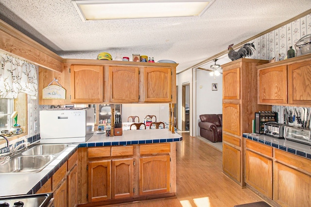 kitchen featuring tile countertops, stove, sink, light wood-type flooring, and a textured ceiling