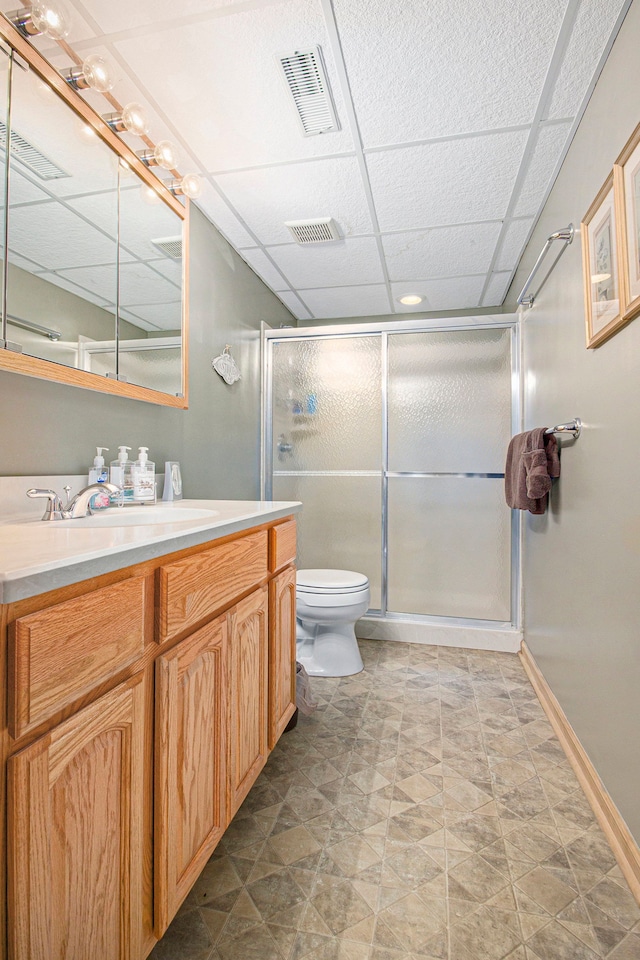 bathroom featuring toilet, vanity, a drop ceiling, and walk in shower