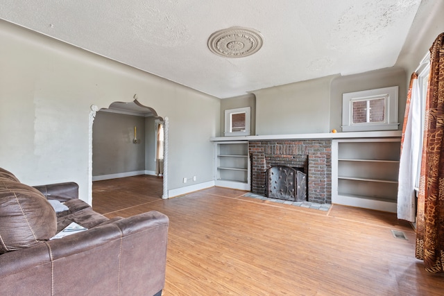 living room with hardwood / wood-style floors, a textured ceiling, and a brick fireplace