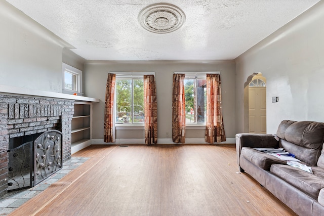 living room with a textured ceiling, built in features, light wood-type flooring, and a fireplace