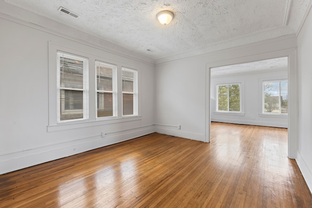 empty room featuring wood-type flooring, a textured ceiling, and crown molding