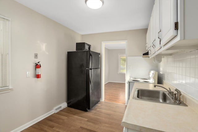 kitchen featuring sink, backsplash, light hardwood / wood-style floors, white cabinets, and black appliances