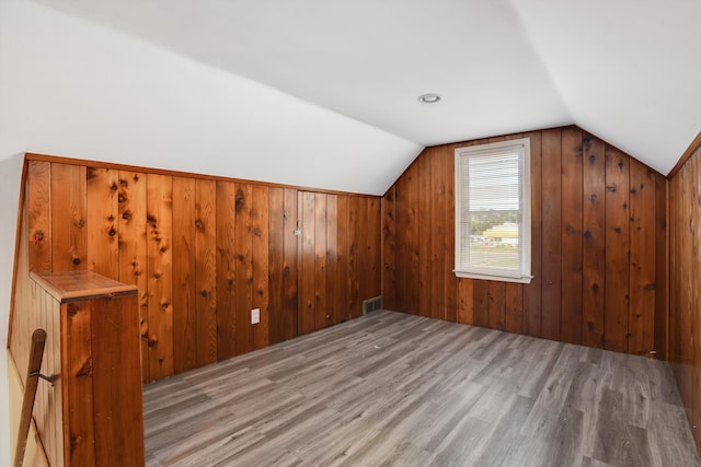 additional living space with wood walls, vaulted ceiling, and light wood-type flooring