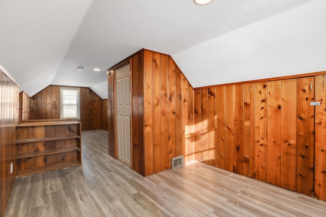 additional living space with wood walls, light hardwood / wood-style flooring, and vaulted ceiling