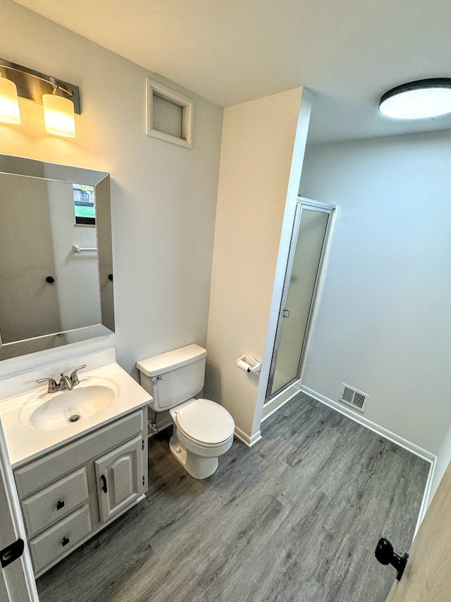 bathroom with wood-type flooring, vanity, toilet, and a shower with shower door