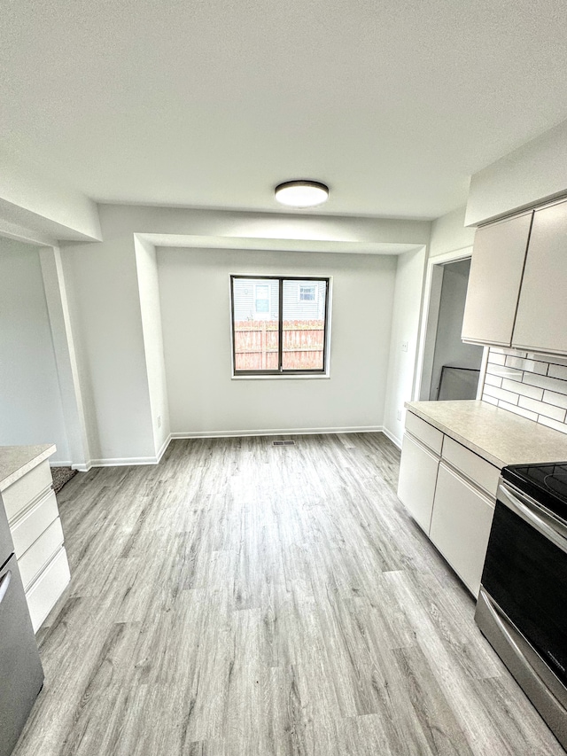 kitchen featuring backsplash, white cabinets, a textured ceiling, light hardwood / wood-style floors, and stainless steel range oven