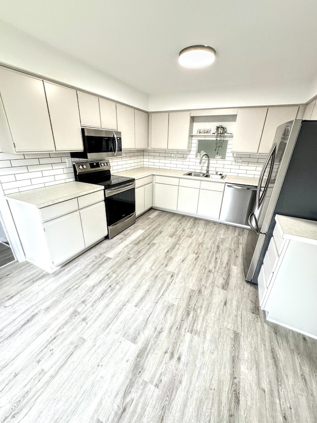 kitchen featuring white cabinetry, sink, stainless steel appliances, light hardwood / wood-style flooring, and backsplash