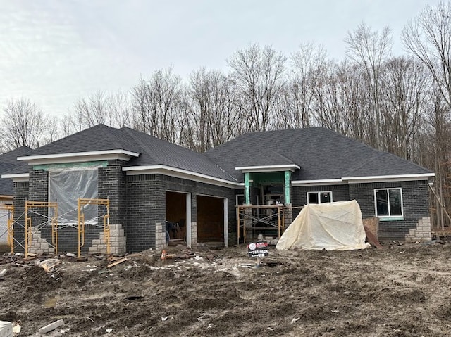 rear view of property with brick siding, an attached garage, and a shingled roof