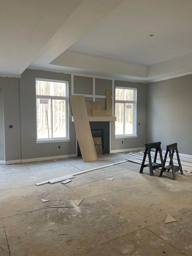 unfurnished living room with a wealth of natural light, a glass covered fireplace, baseboards, and a tray ceiling