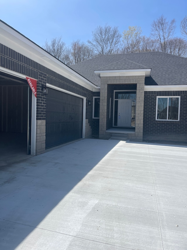 view of front of house with a shingled roof, an attached garage, driveway, and brick siding
