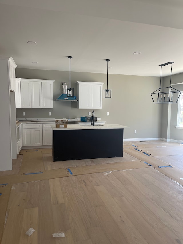 kitchen featuring baseboards, white cabinets, a sink, light wood finished floors, and exhaust hood