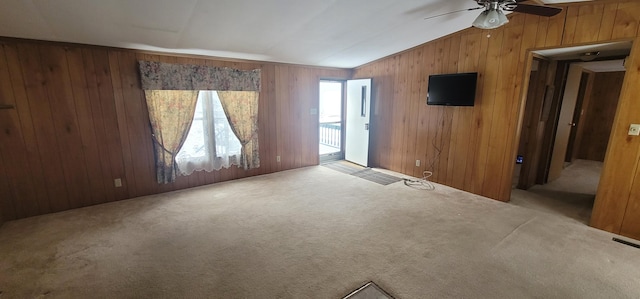 carpeted empty room with ceiling fan, lofted ceiling, and wood walls