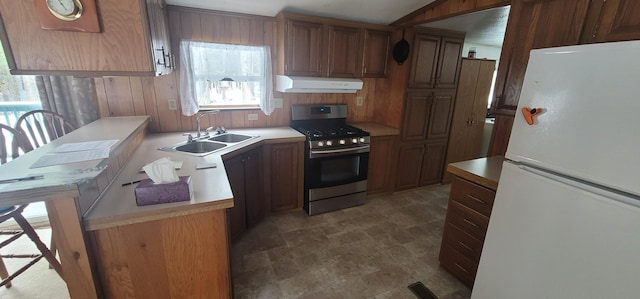 kitchen featuring wood walls, white fridge, stainless steel range with gas cooktop, and sink