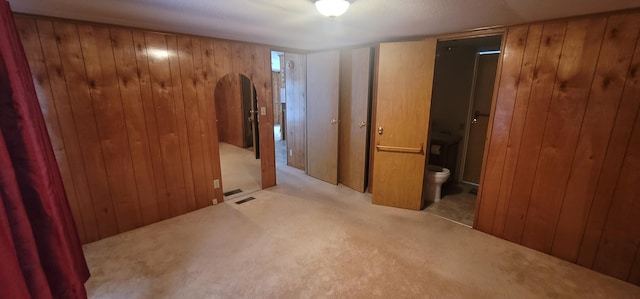 unfurnished bedroom with light carpet, ensuite bathroom, and wood walls