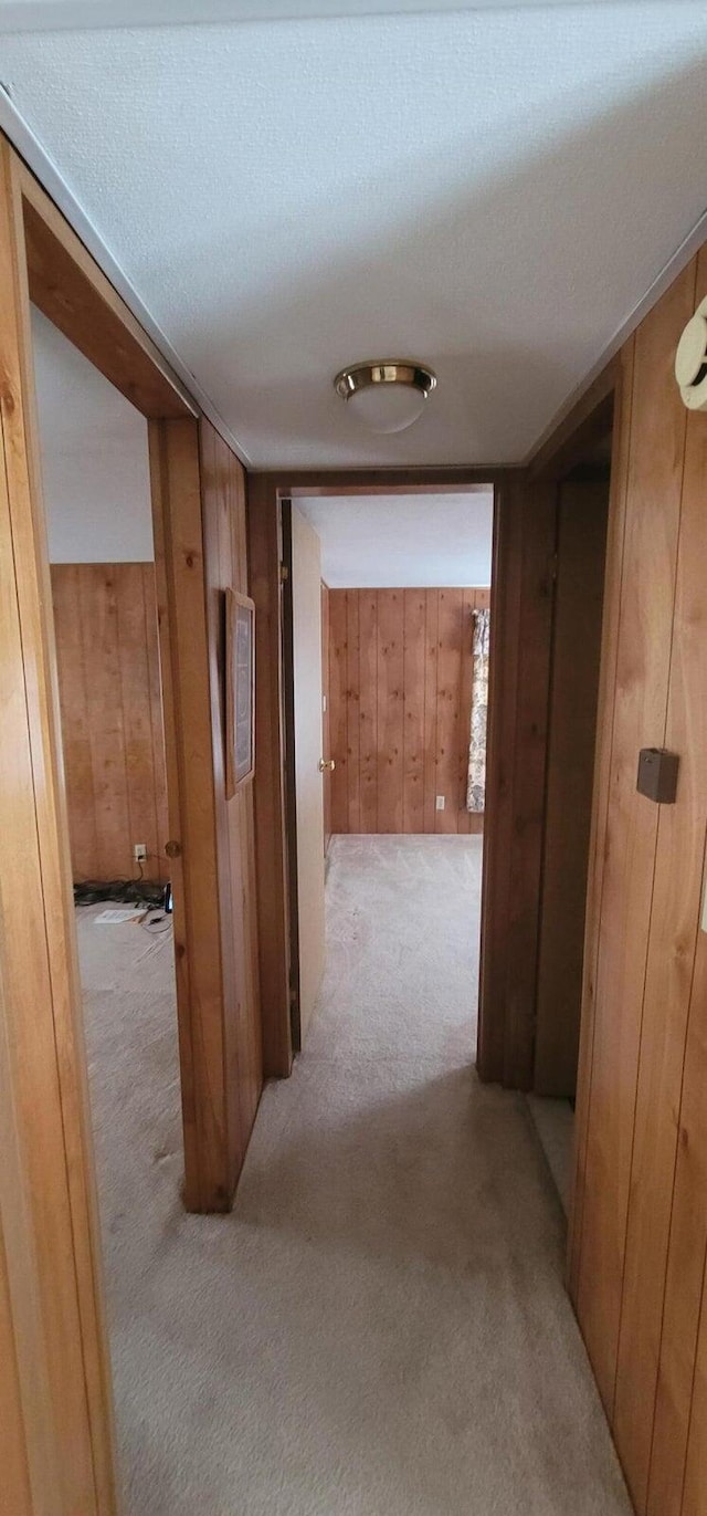 hallway with wooden walls, light colored carpet, and a textured ceiling