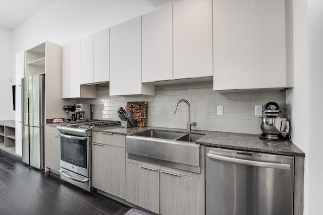 kitchen featuring sink, dark wood-type flooring, dark stone counters, decorative backsplash, and appliances with stainless steel finishes