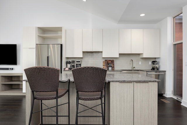 kitchen with appliances with stainless steel finishes, a kitchen island, dark stone countertops, dark hardwood / wood-style floors, and white cabinetry