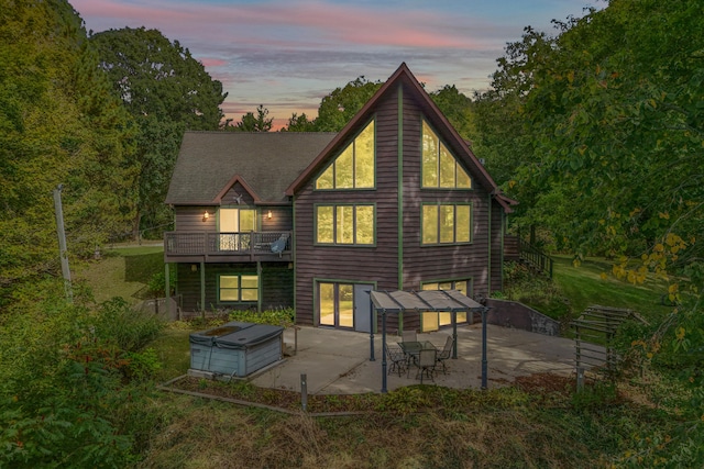 back house at dusk with a balcony and a patio