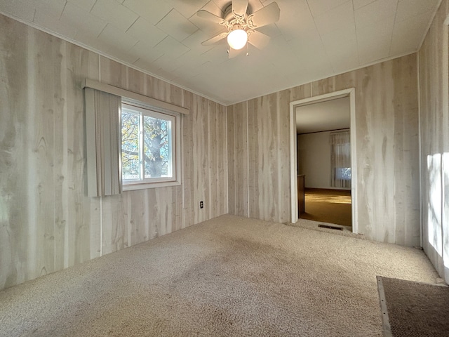 carpeted spare room with ceiling fan and wooden walls