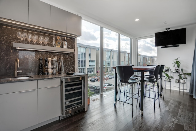 bar featuring decorative backsplash, sink, wine cooler, and dark wood-type flooring