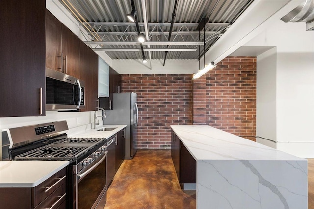 kitchen featuring brick wall, appliances with stainless steel finishes, light stone counters, and sink