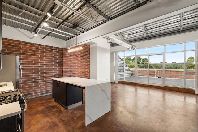 kitchen featuring hanging light fixtures, white gas range, stainless steel refrigerator, light stone counters, and brick wall