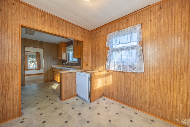 kitchen with dishwasher, sink, crown molding, and wood walls