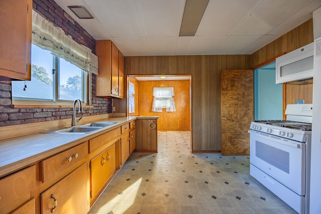 kitchen featuring wood walls, white appliances, sink, and brick wall