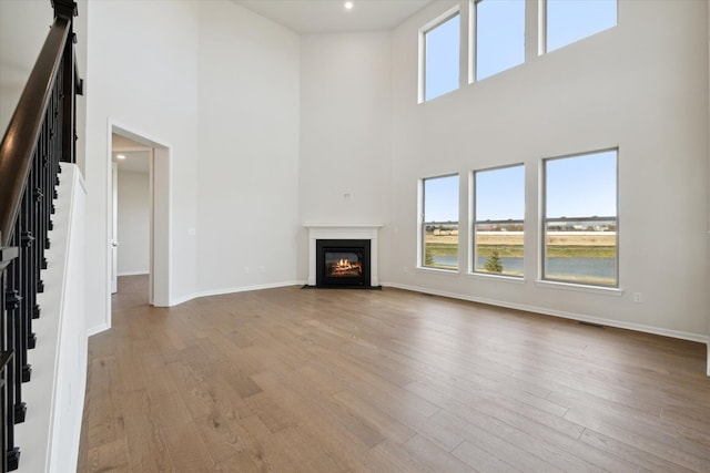 unfurnished living room with baseboards, a fireplace with flush hearth, stairs, light wood-type flooring, and a towering ceiling