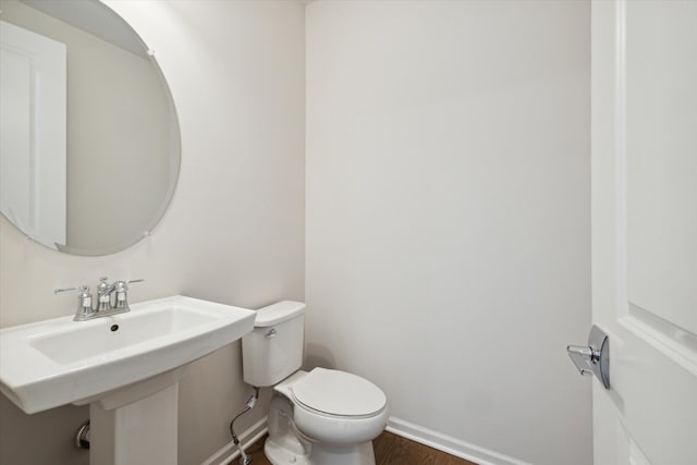 half bathroom with toilet, wood finished floors, baseboards, and a sink