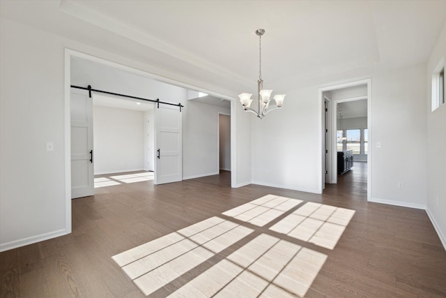 unfurnished dining area featuring dark wood-type flooring, a barn door, baseboards, an inviting chandelier, and a raised ceiling