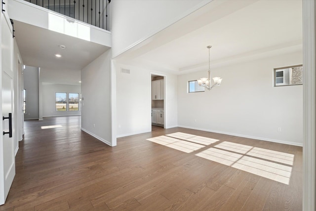 unfurnished room featuring a barn door, baseboards, dark wood-type flooring, and a notable chandelier