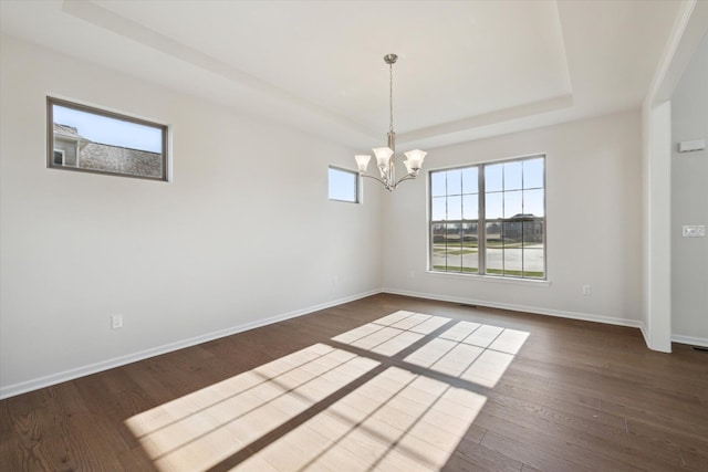 spare room featuring a tray ceiling, a notable chandelier, baseboards, and dark wood-style flooring