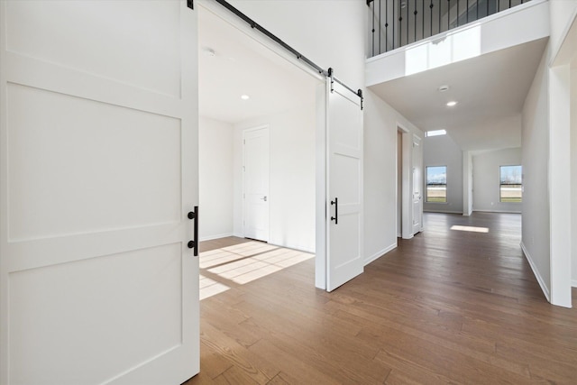 corridor with a barn door, baseboards, wood finished floors, and a towering ceiling