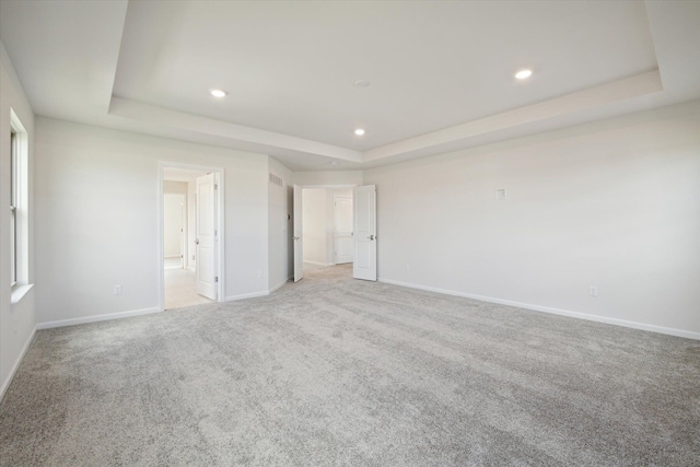 unfurnished bedroom featuring baseboards, recessed lighting, ensuite bathroom, light carpet, and a raised ceiling