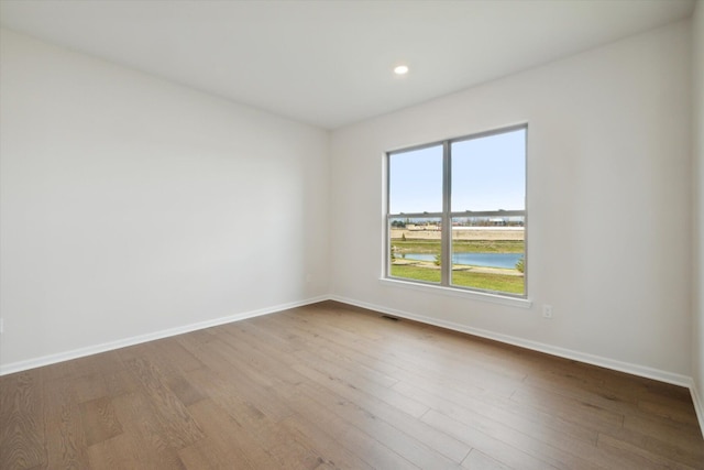 empty room with visible vents, baseboards, wood finished floors, and a water view