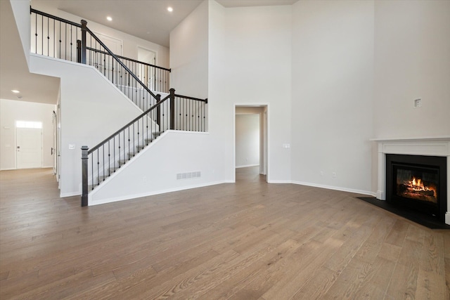 unfurnished living room with a fireplace with flush hearth, stairs, baseboards, and wood finished floors