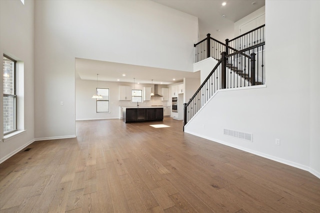 unfurnished living room with visible vents, baseboards, wood finished floors, and stairs
