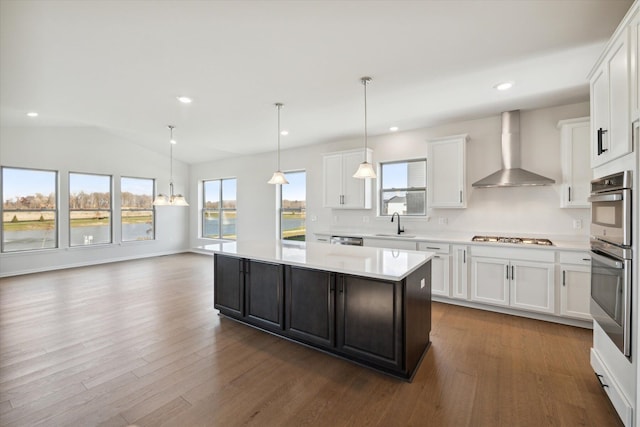 kitchen featuring wall chimney range hood, light countertops, white cabinets, stainless steel appliances, and a sink