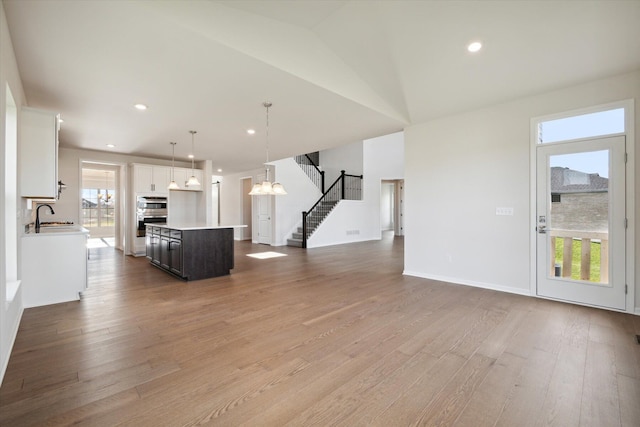 unfurnished living room featuring a sink, plenty of natural light, stairs, and light wood finished floors