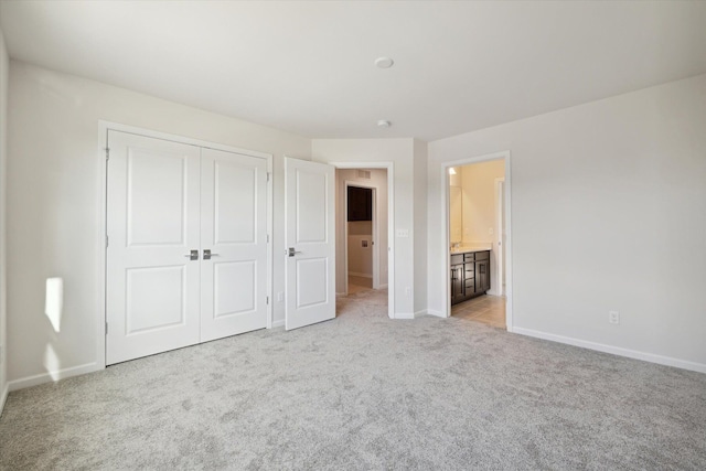 unfurnished bedroom with ensuite bath, baseboards, a closet, and light carpet