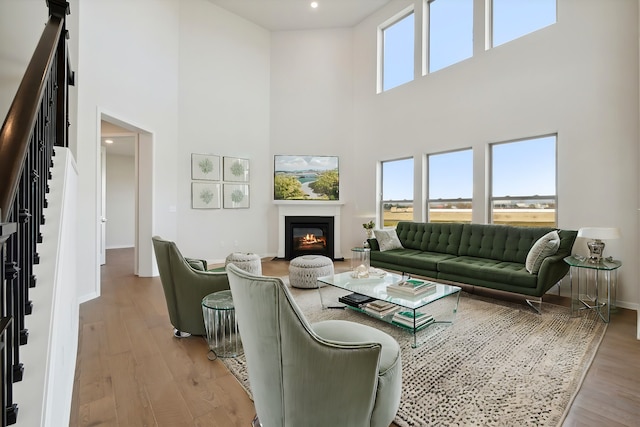 living area featuring a glass covered fireplace, baseboards, light wood-style flooring, and stairs