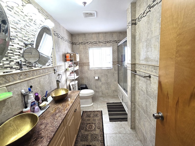 full bathroom with vanity, shower / bath combination with glass door, tile patterned floors, toilet, and tile walls