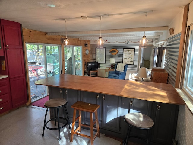 kitchen featuring a kitchen bar, wooden walls, hanging light fixtures, and wood counters