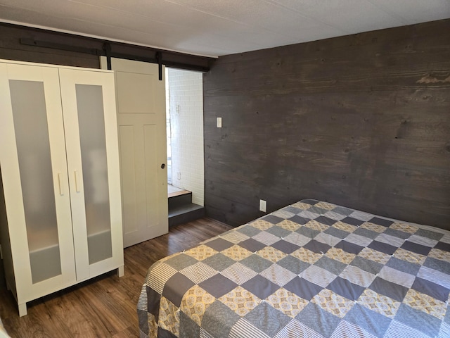 unfurnished bedroom featuring a closet, a barn door, wooden walls, and dark hardwood / wood-style flooring