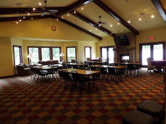 carpeted dining space featuring ceiling fan, beam ceiling, a stone fireplace, and high vaulted ceiling