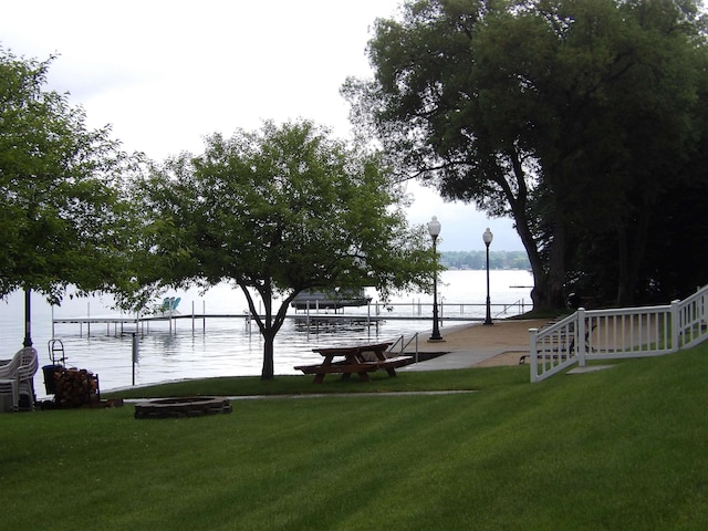 view of property's community with a lawn, a boat dock, a water view, and an outdoor fire pit